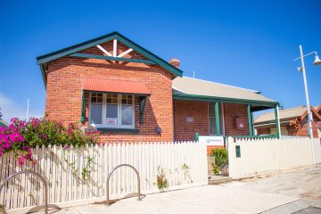 A charming red brick house with a well-maintained garden and a clear blue sky in the background.