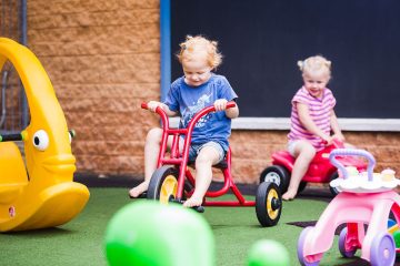 A young boy plays with a toy in a bright classroom filled with educational materials and colourful decorations.